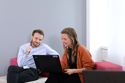 Zwei Mitarbeitende sitzen im Gespräch vor einem Laptop