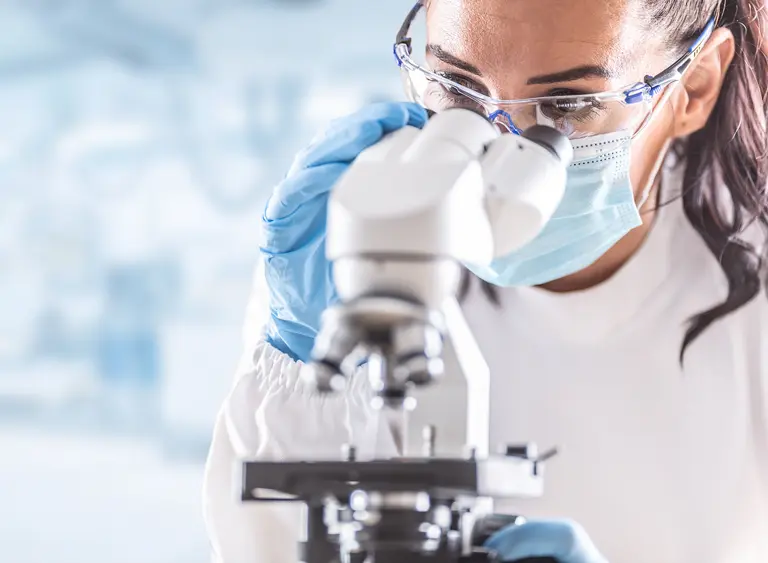 Eine Forscherin mit Schutzkleidung schaut in ein Mikroskop
